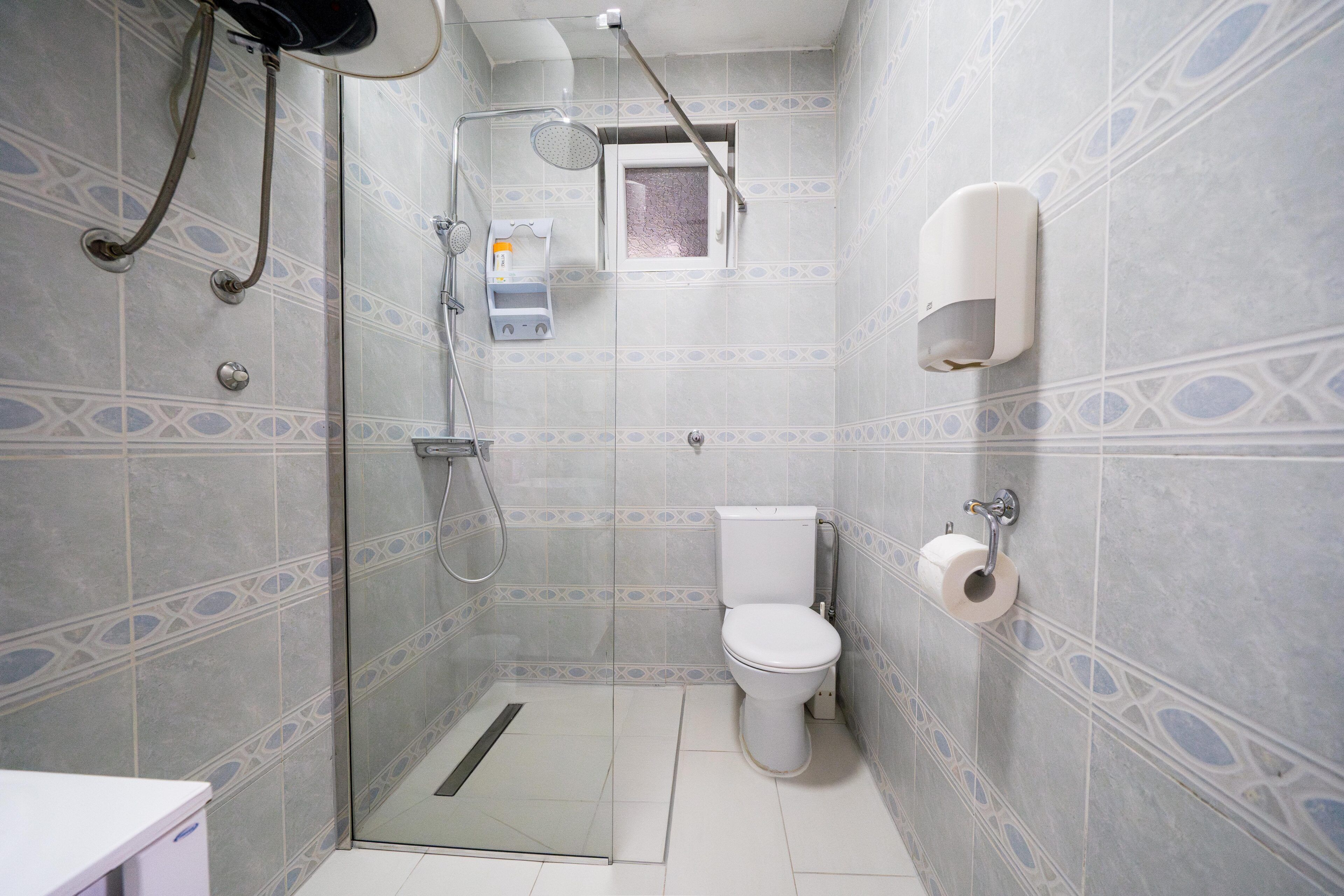 Baño con ducha, inodoro y secamanos.