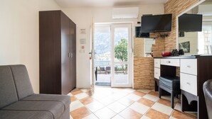 Habitación de hotel con sofá, escritorio con silla, televisor montado en la pared y puerta corrediza de vidrio que da a un área exterior con mesa y sillas.