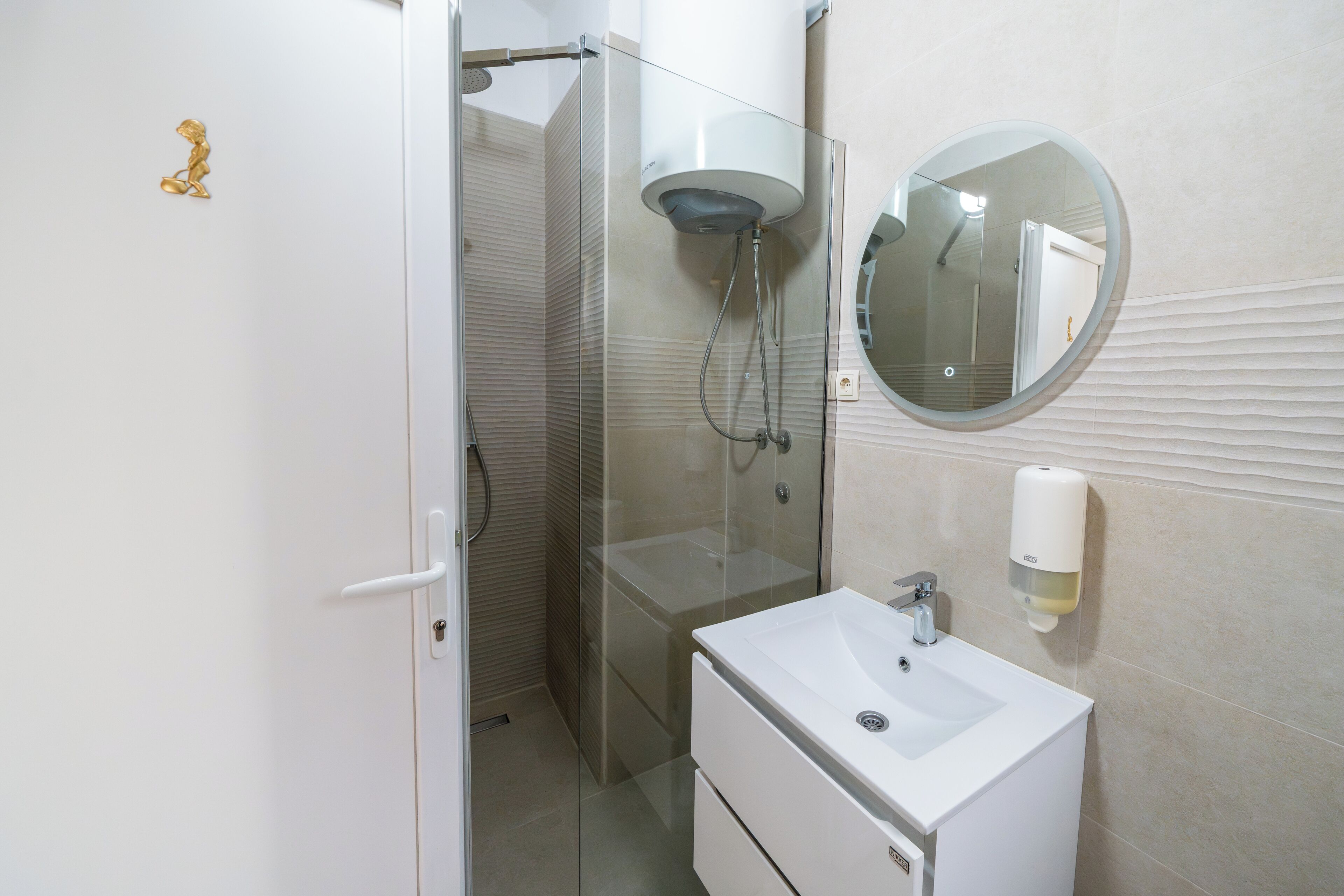 Ein Badezimmer mit einer gläsernen Duschkabine, einem weißen Waschbecken und einem runden Spiegel an der Wand.