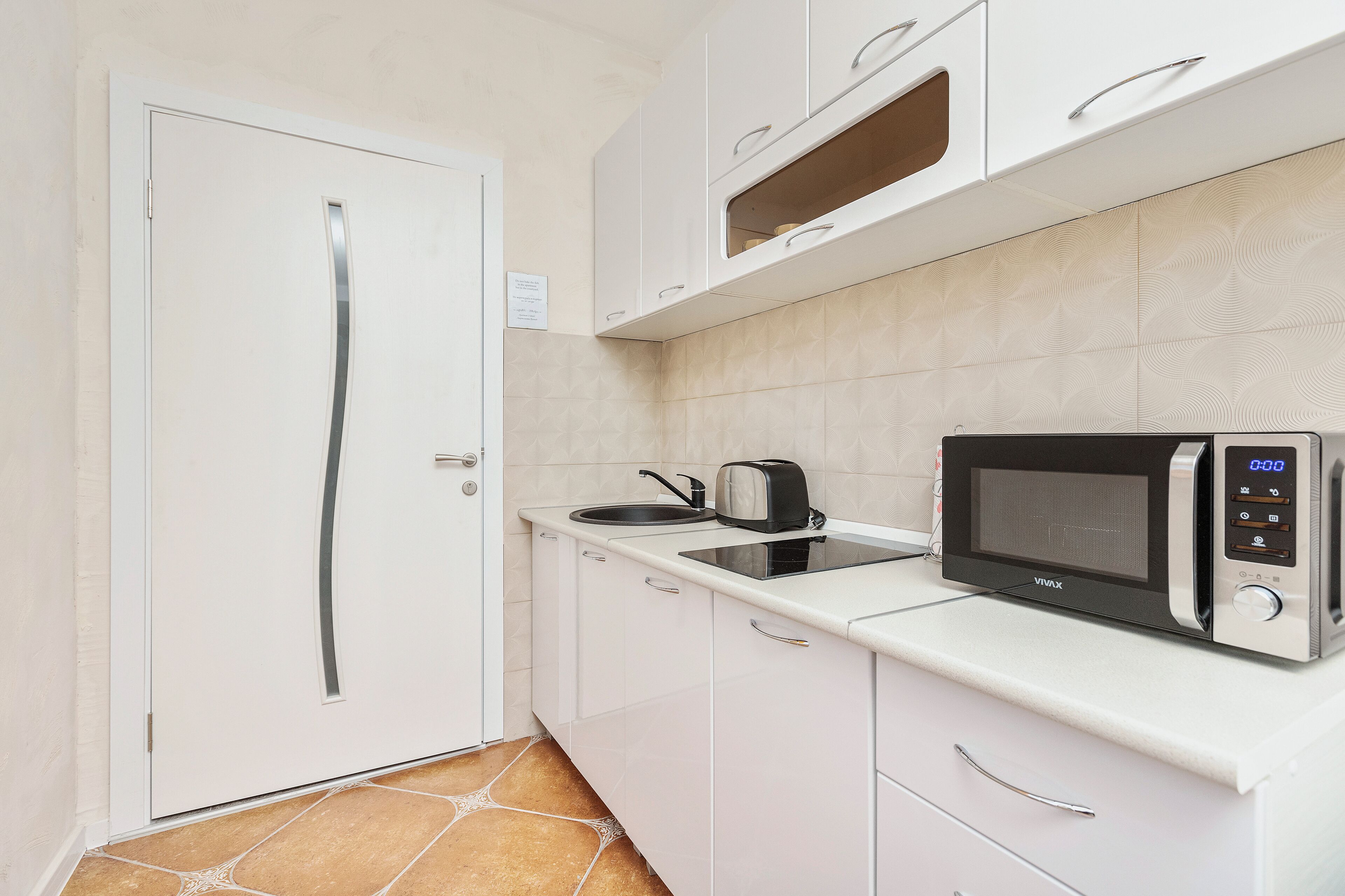 Une cuisine compacte avec des meubles blancs, un four à micro-ondes, un grille-pain et une bouilloire posés sur le plan de travail.