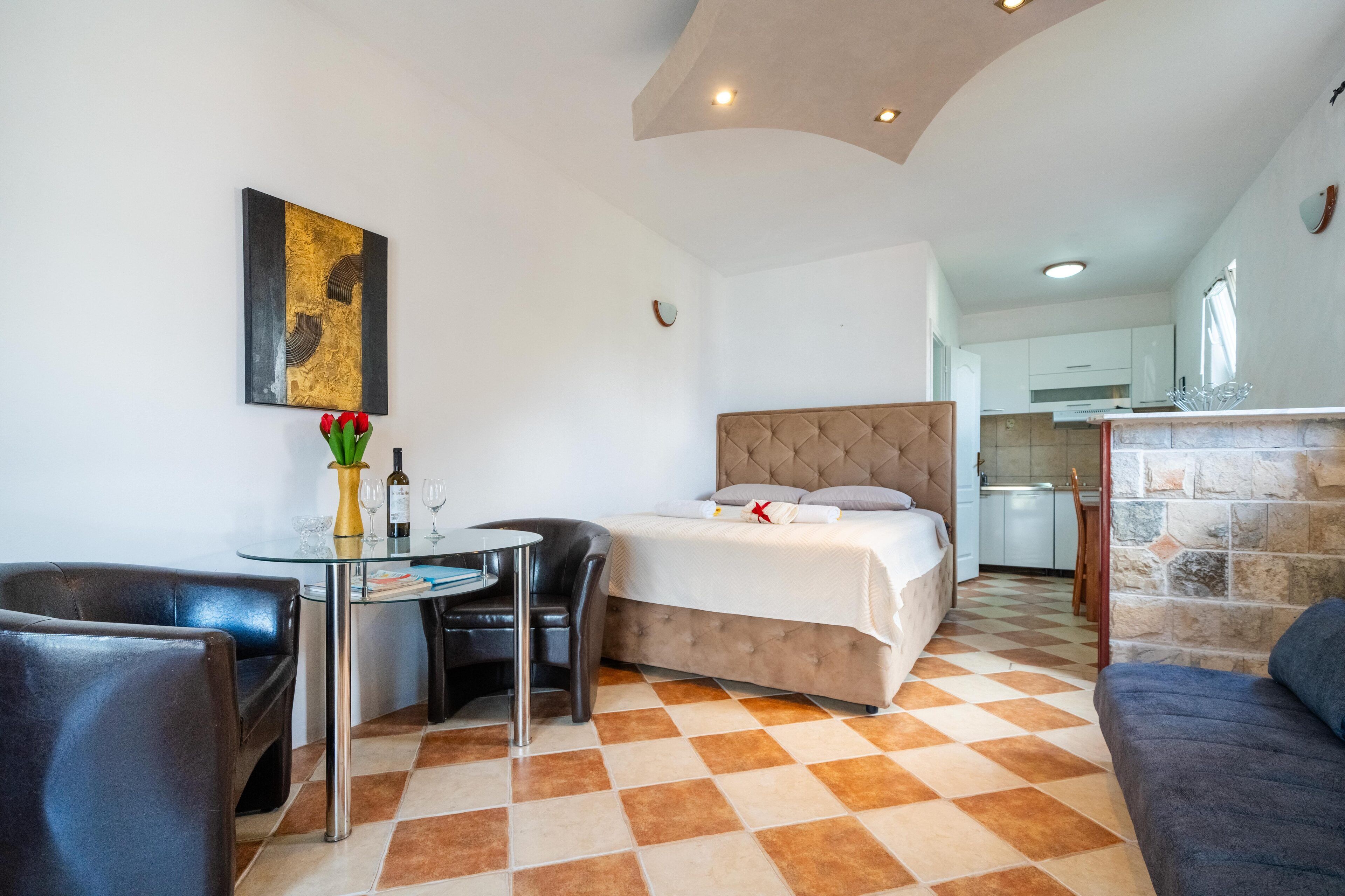 A hotel room with a bed, a dining table with chairs, a small kitchen area, and a checkered floor.