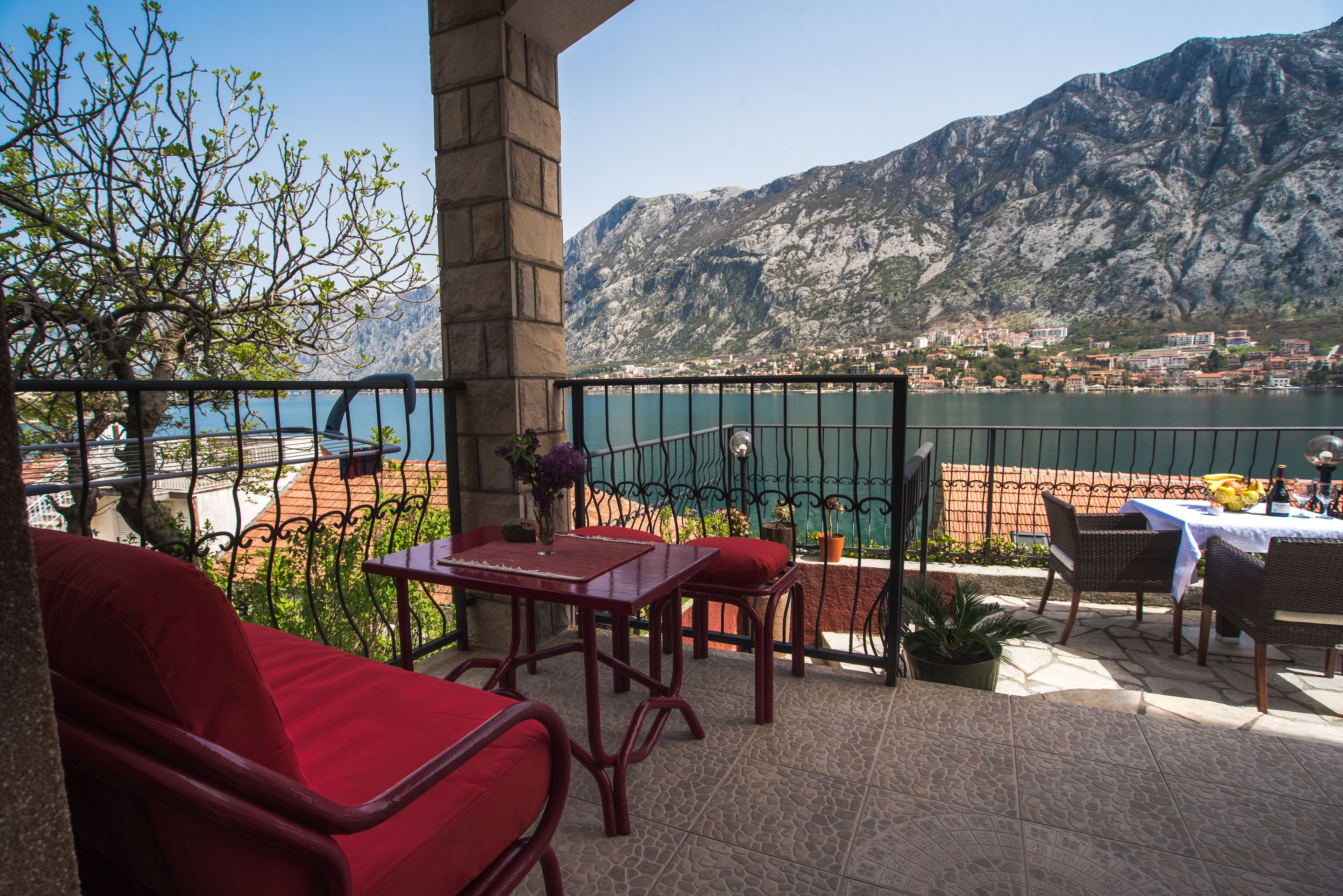 A terrace with red furniture, a table with a vase, and a view of a lake and mountains.