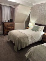 Un dormitorio con cama, cómoda, mesita de noche, lámpara y un papel tapiz estampado.