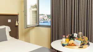 Quarto de hotel com cama, uma pequena mesa com itens de café da manhã, uma janela com vista para prédios e uma cortina.