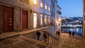 Um edifício histórico com fachada de pedra, várias janelas e uma escadaria que leva a uma varanda com vista para um rio.