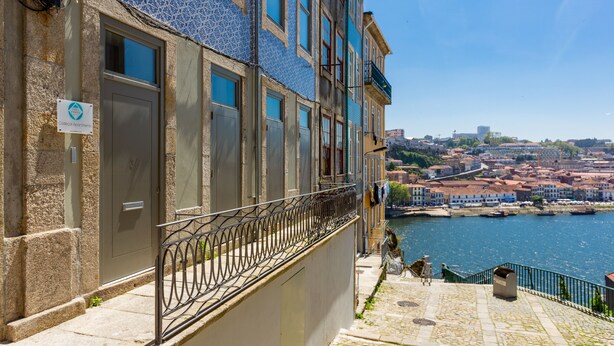 Um edifício com fachada em azulejos, guarda-corpo de metal e vista para um rio e horizonte urbano.