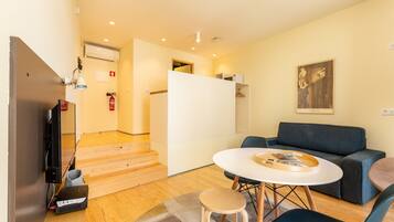 Un salon moderne avec un canapé, une table ronde et un téléviseur. Un escalier mène à une autre pièce.