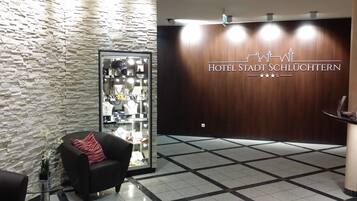 A reception area with a stone wall, a glass display case with jewelry, a black armchair, and a wooden wall with the hotel name.