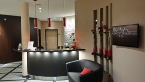 Un espace d’accueil avec un comptoir noir, un vase rouge, une chaise noire avec un coussin rouge et un panneau fixé au mur.