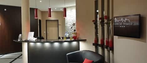 Zona de recepción con mostrador negro, un florero rojo, una silla negra con cojín rojo y un letrero en la pared.
