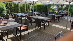 Un café en plein air avec des tables et des chaises disposées sous des auvents, entouré de verdure.