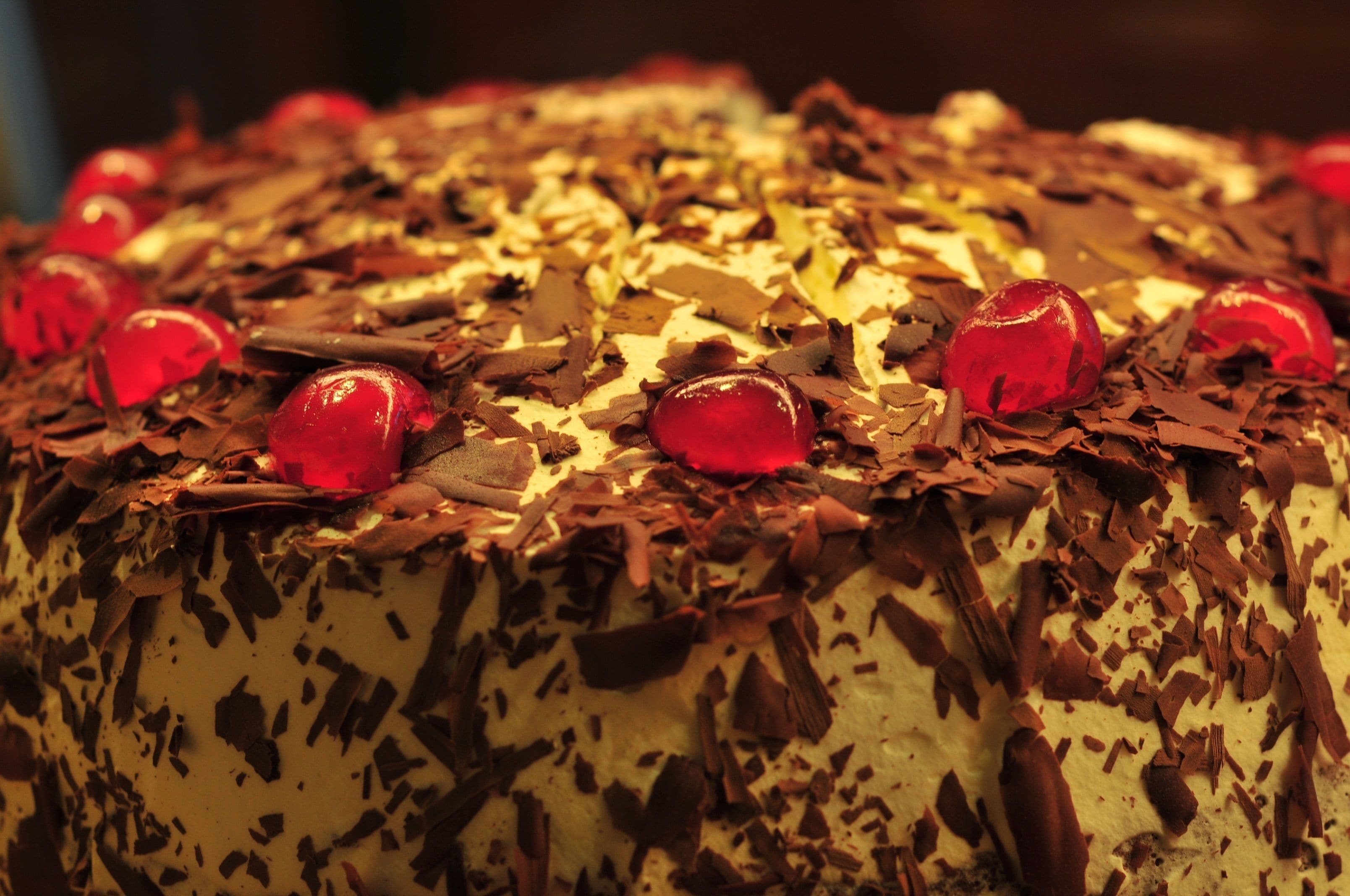 A cake with chocolate shavings and red cherries on top.