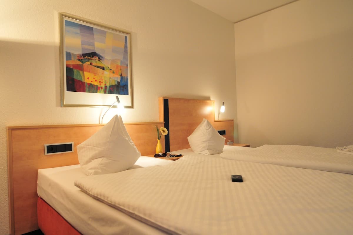 Habitación de hotel con dos camas, un cuadro en la pared y una mesita de noche con una lámpara.