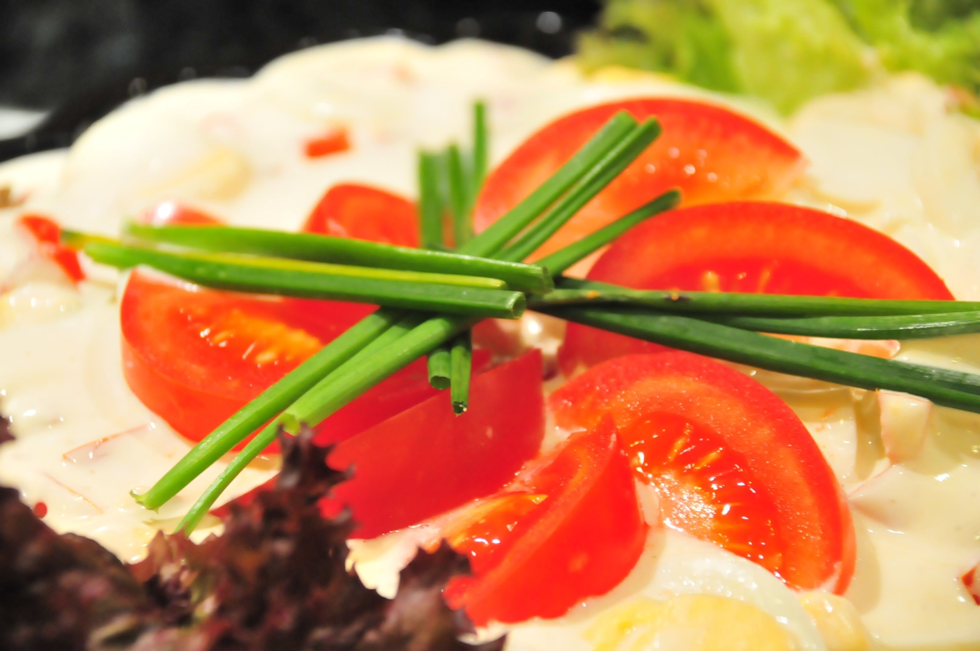 A close-up of a dish with sliced tomatoes, green onions, and a creamy sauce.