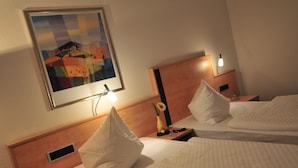 Une chambre d’hôtel avec deux lits, une table de chevet avec une lampe, un tableau encadré au mur et un petit vase avec une fleur.