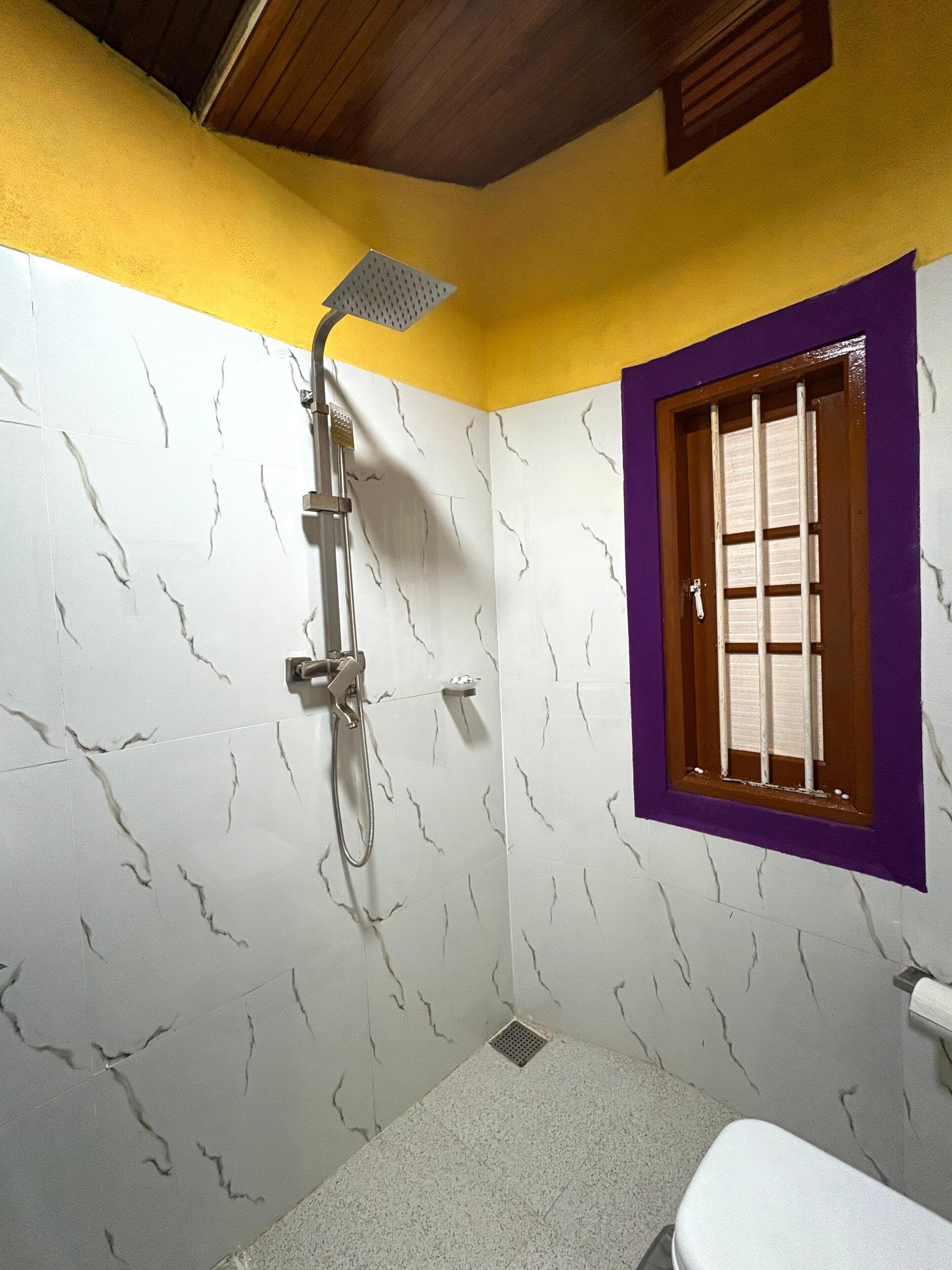 Un baño con ducha, una ventana con barrotes y un inodoro.