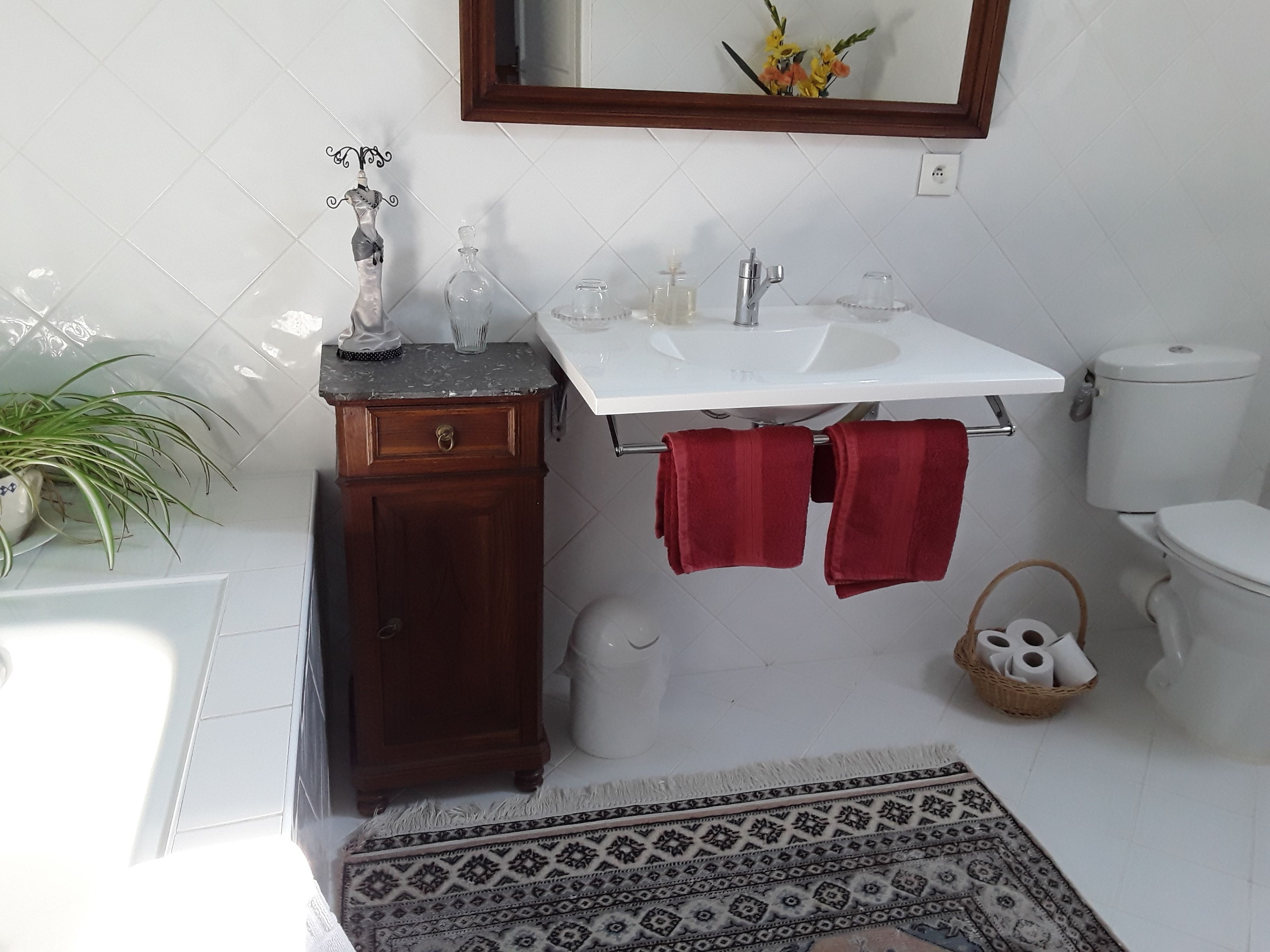 A bathroom with a white sink, wooden cabinet, red towels, a mirror, and a patterned rug.