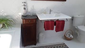 A bathroom with a white sink, wooden cabinet, red towels, a mirror, and a patterned rug.