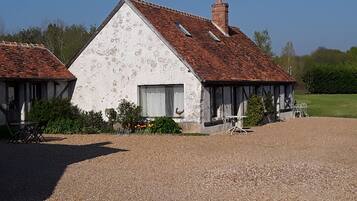 A rustic building with a sloped roof and a chimney, surrounded by a gravel driveway and a small garden area with outdoor furniture.