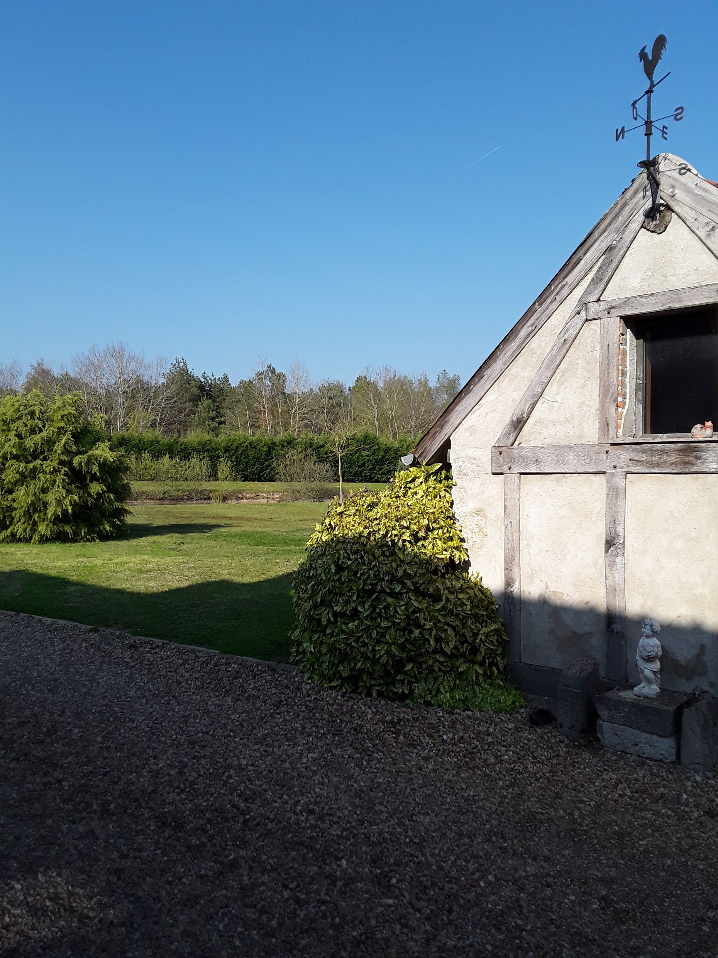 A rustic building with a weather vane, surrounded by a well-maintained lawn and a hedge.