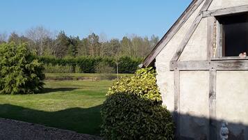 A rustic building with a weather vane, surrounded by a well-maintained lawn and a hedge.
