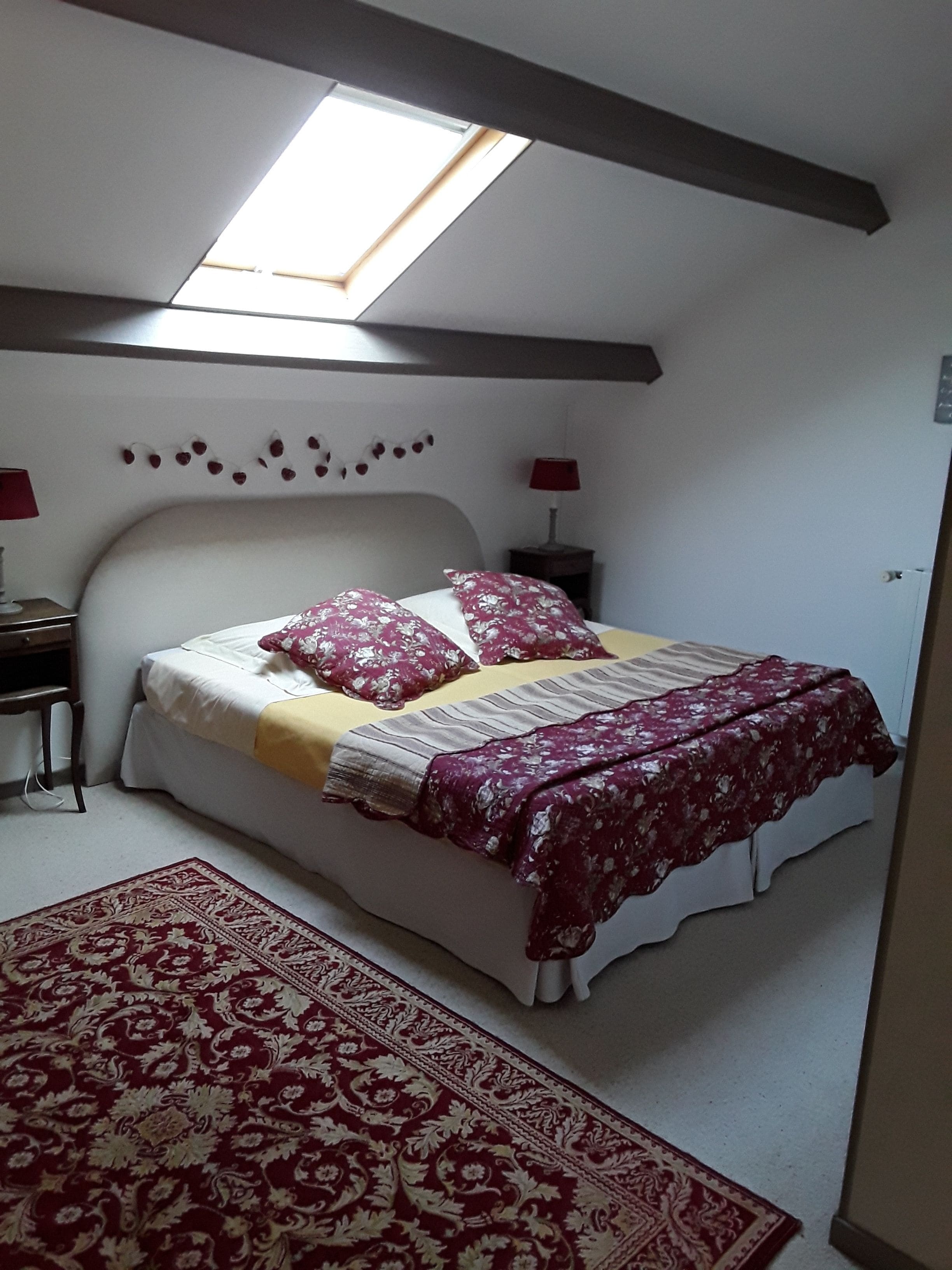 Une chambre avec un puits de lumière, un lit avec une literie à motifs floraux, une table de chevet avec une lampe et un tapis à motifs.