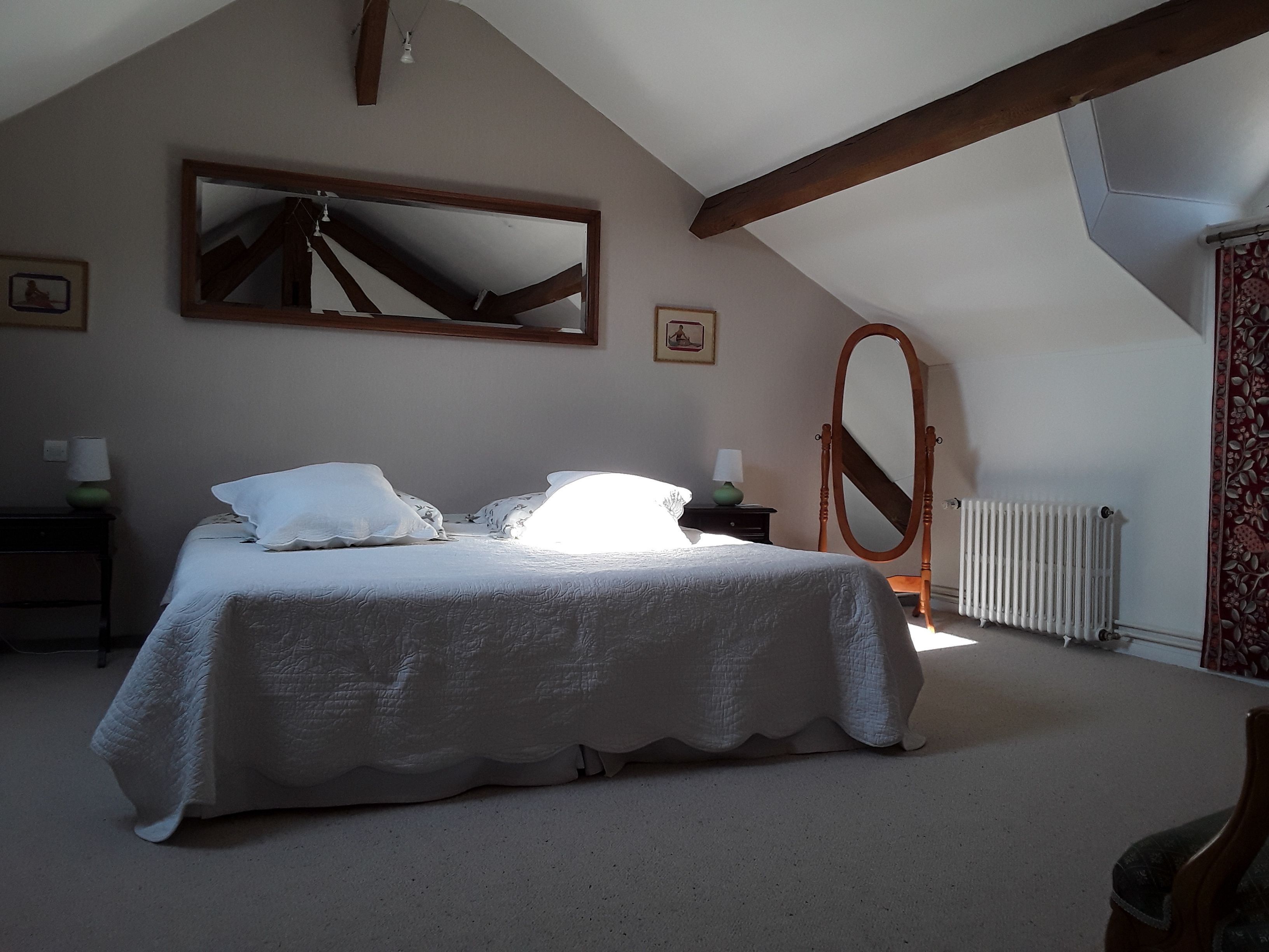 A bedroom with a large bed, a wooden ceiling beam, a mirror, and a radiator.