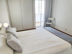 A bedroom with a bed, a chair, a nightstand, and a window with curtains.
