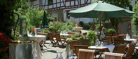 An outdoor café with wooden tables and chairs, green umbrellas, and potted plants.