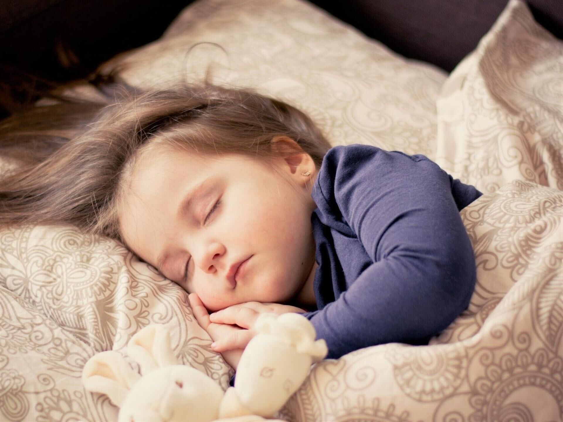 A child sleeping on a patterned bed with a teddy bear.