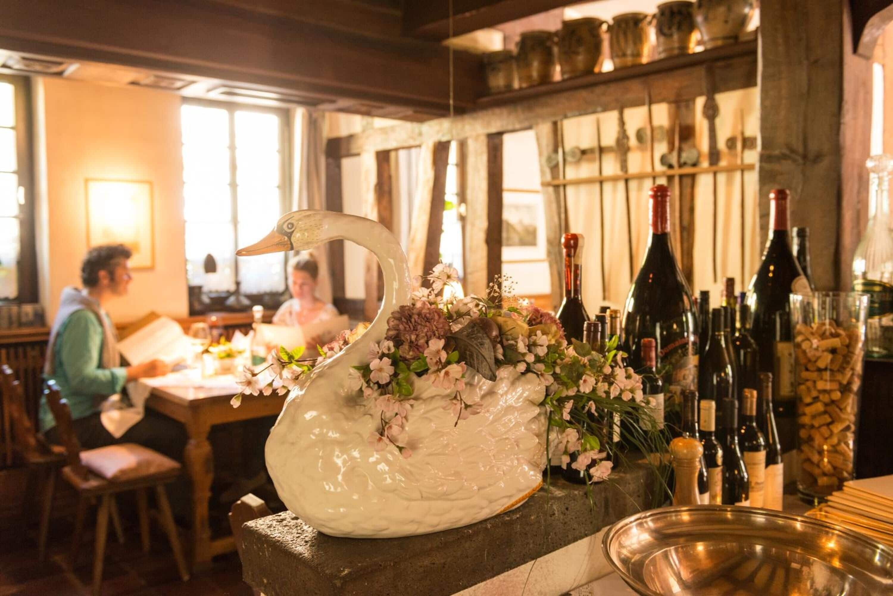 A restaurant interior with a large white swan centerpiece, wooden tables, and a variety of wine bottles.