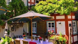 A traditional European courtyard with a stone building, a wooden table with chairs, and a large umbrella. - Hotel Landgasthof Zum Weissen Schwanen (Braubach)