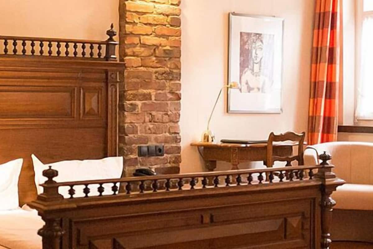 Un lit en bois avec une tête de lit, une chaise, un bureau et un mur en pierre.