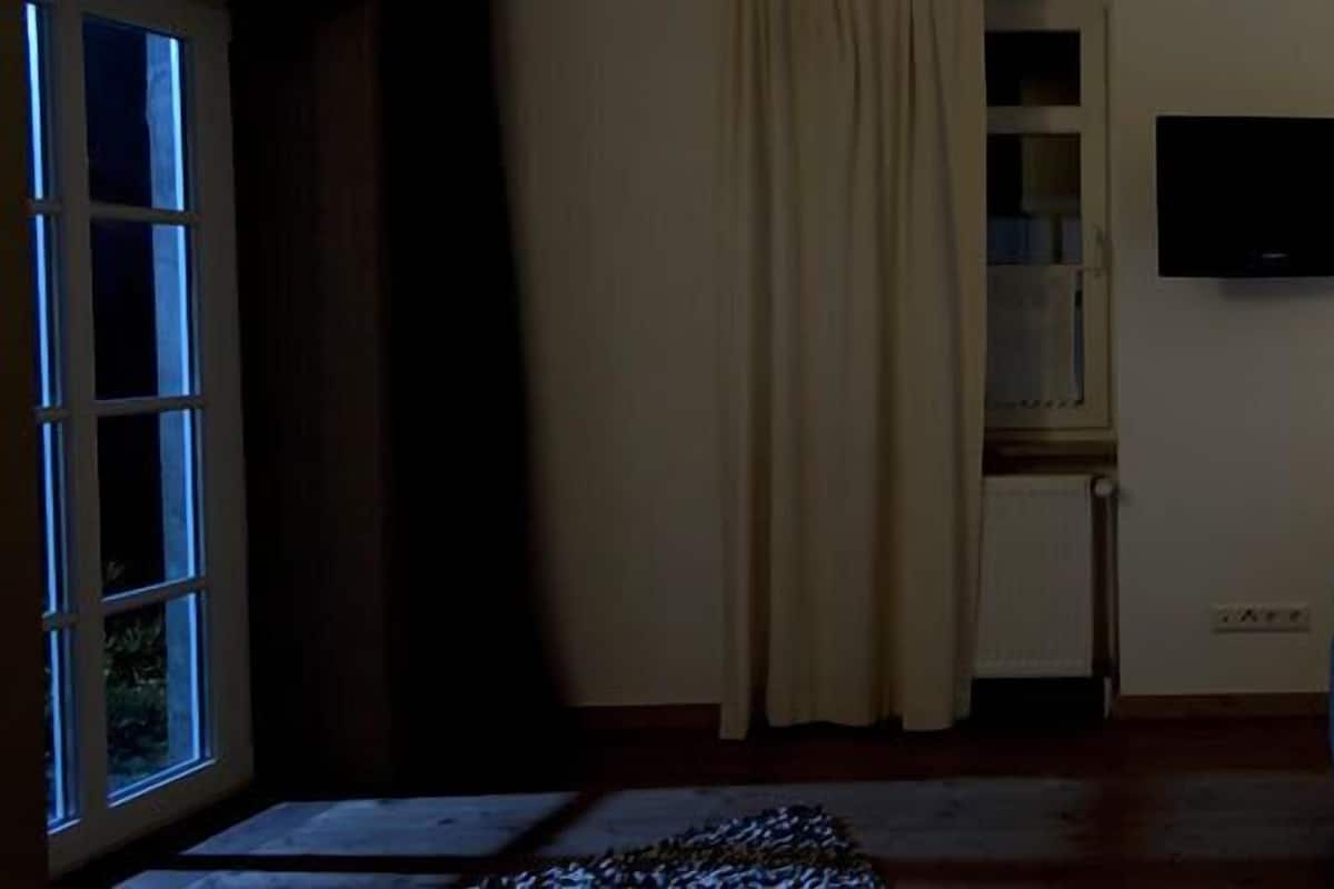 Une chambre à coucher avec un lit, une fenêtre, un téléviseur fixé au mur et une lampe de chevet.