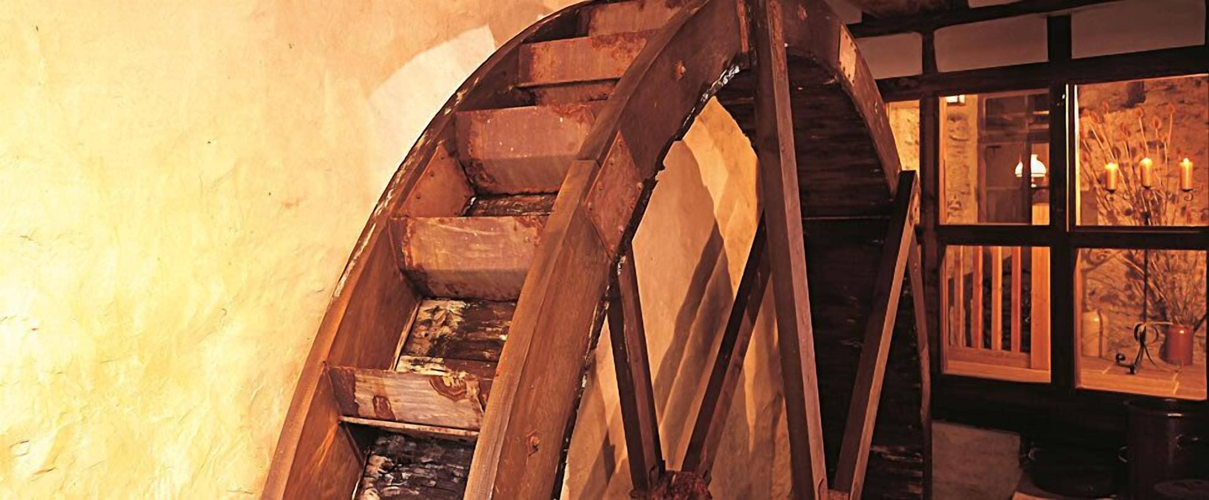 A wooden spiral staircase with a rustic interior, leading to a room with a stone wall and a window with candles.