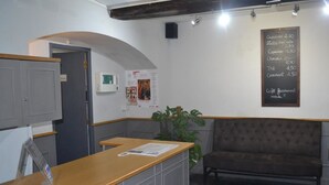 Een receptiebalie van hout, een donkere gestoffeerde bank, een menukaart aan de muur en een plant.