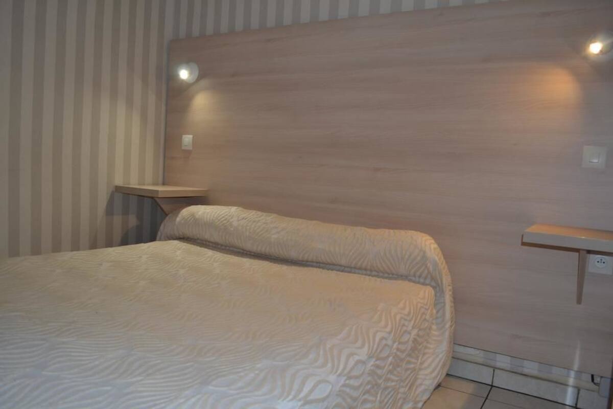 Une chambre à coucher comprenant un lit, une table de chevet, une étagère fixée au mur et un luminaire.