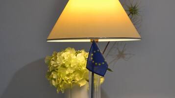 A lamp with a blue flag on a table next to a vase of flowers.