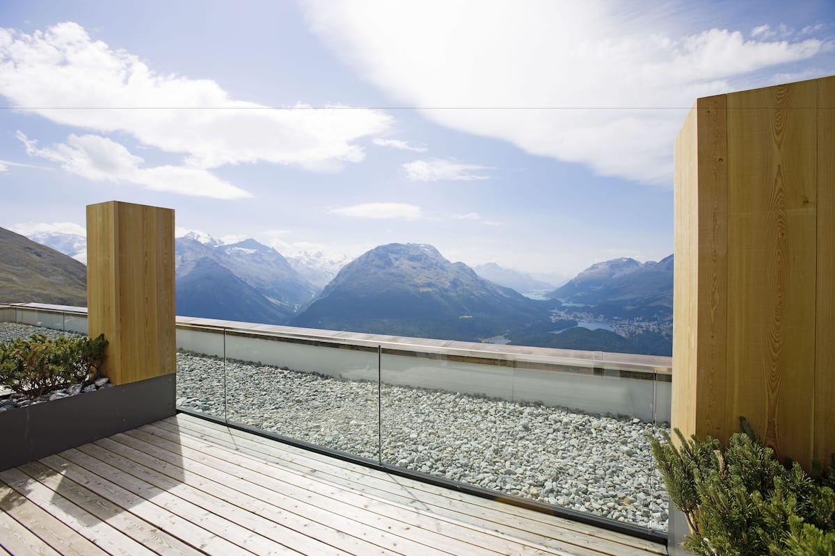 Una terraza de madera con barandilla de vidrio que ofrece vistas a un paisaje montañoso.