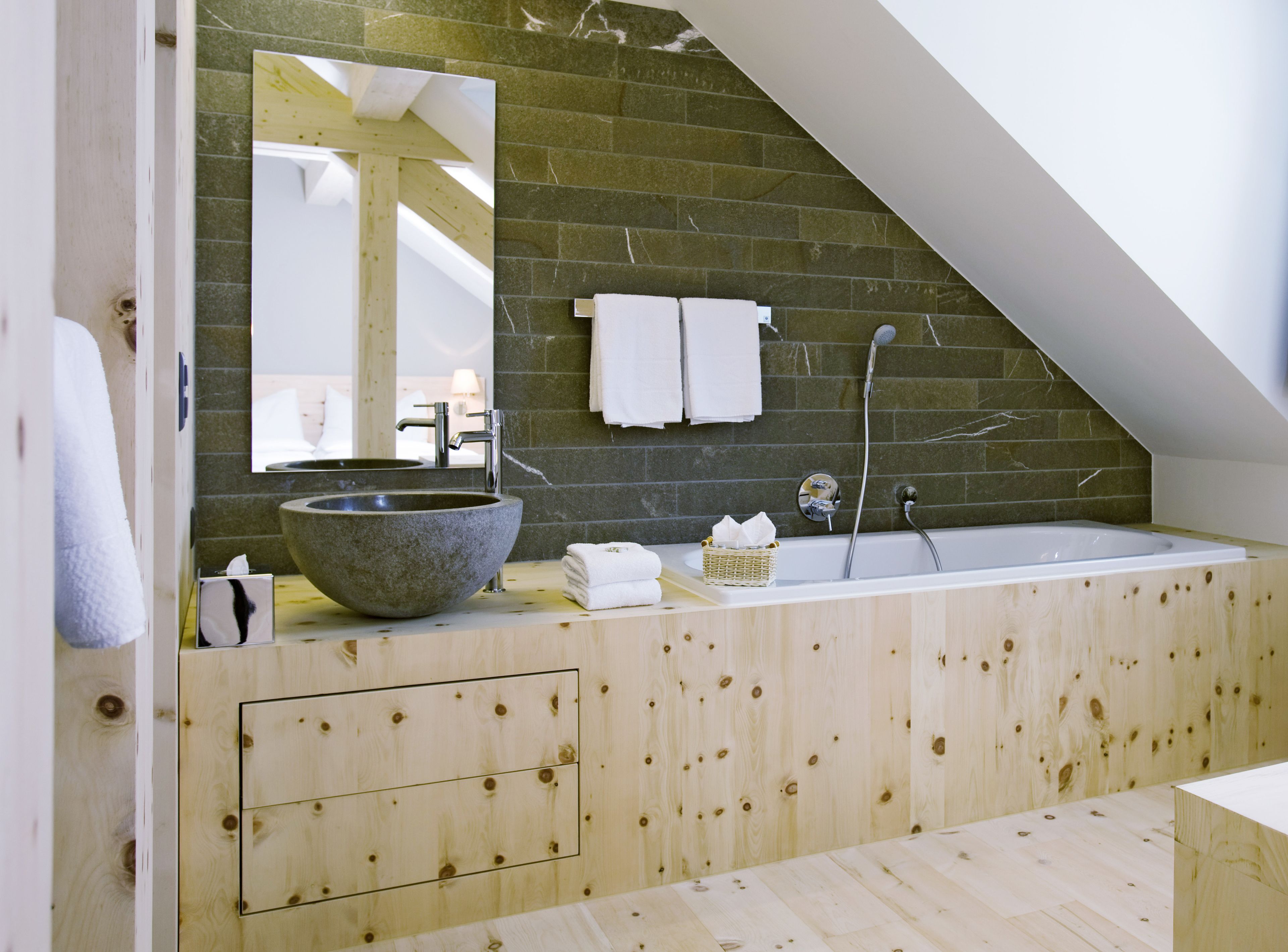 Un baño moderno con un lavamanos de piedra, una bañera independiente y un tocador de madera.