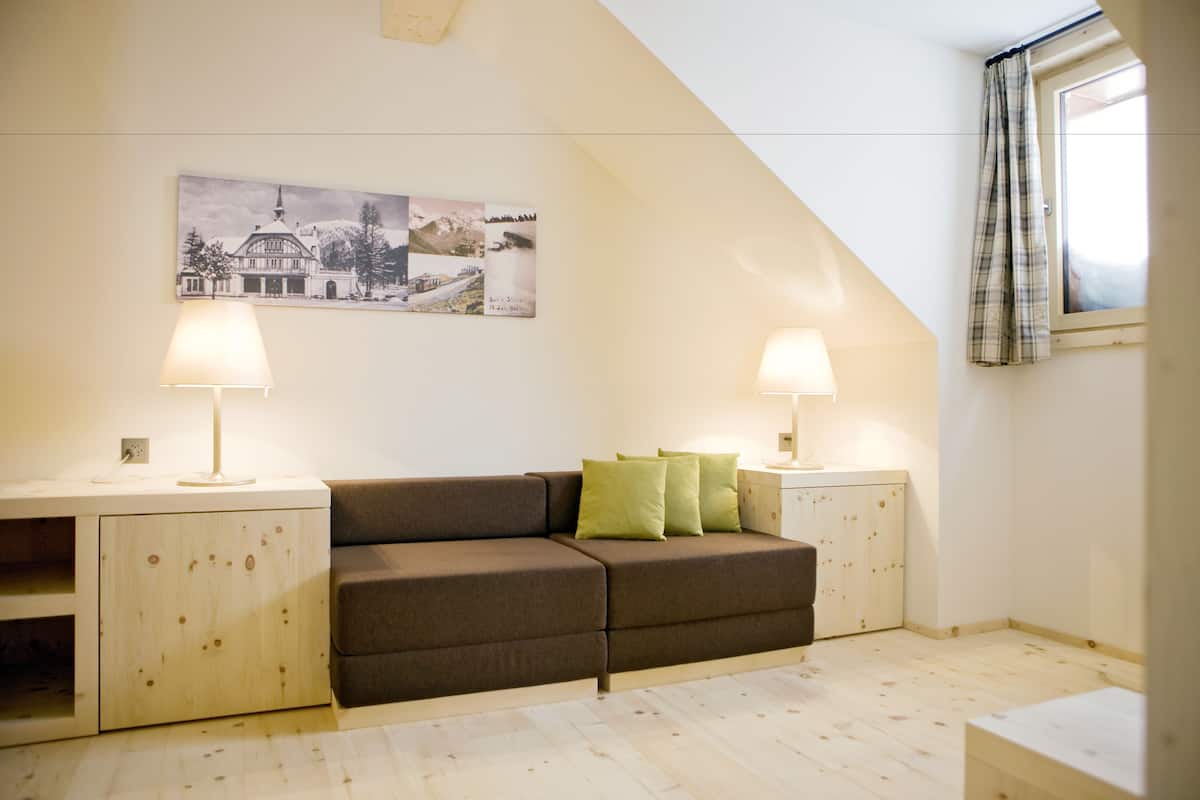 Una habitación acogedora con un sofá marrón, dos mesitas de noche con lámparas, un armario de madera y un cuadro grande en la pared.