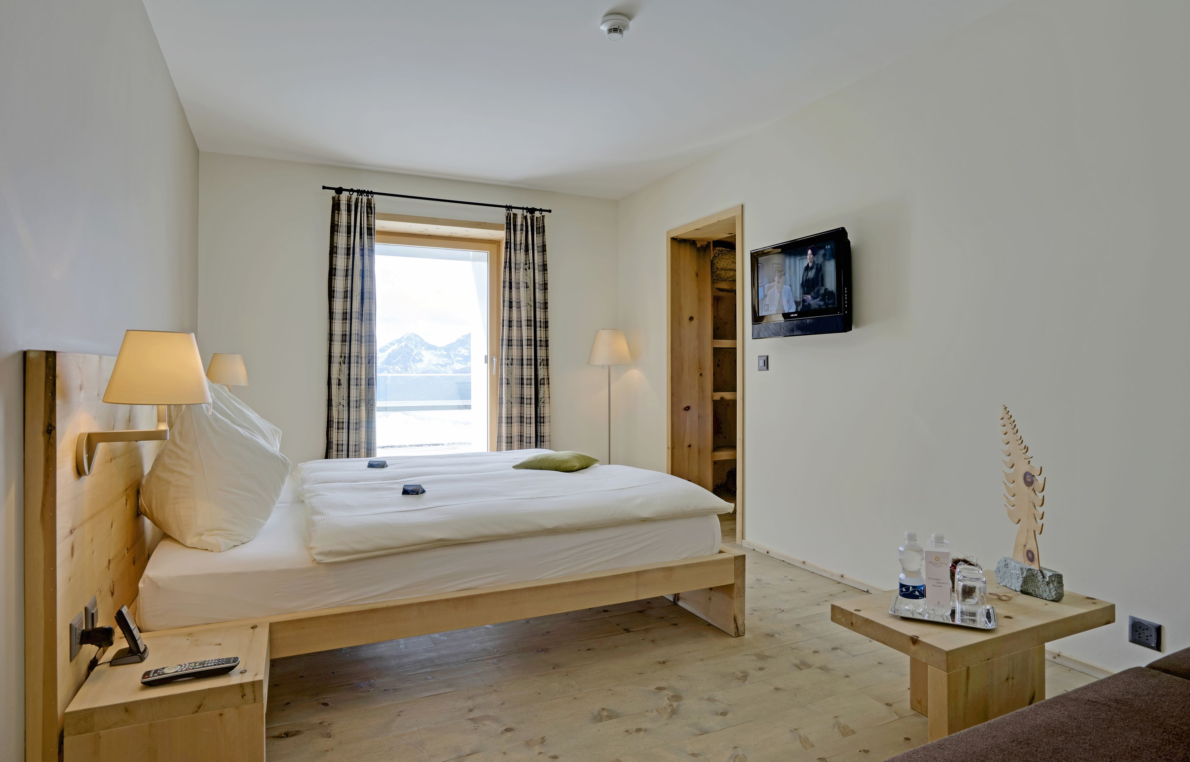 A bedroom with a bed, bedside lamps, a TV, a wooden nightstand, and a small table with items.