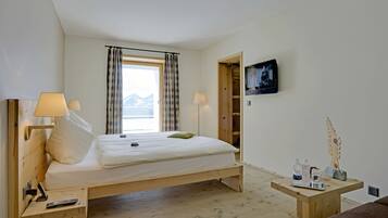A bedroom with a bed, bedside lamps, a TV, a wooden nightstand, and a small table with items.