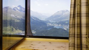 A window with a view of a mountainous landscape, including a valley and a lake.