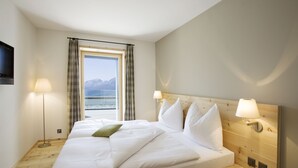 A hotel room with a bed, bedside lamps, a TV, and a window with curtains.