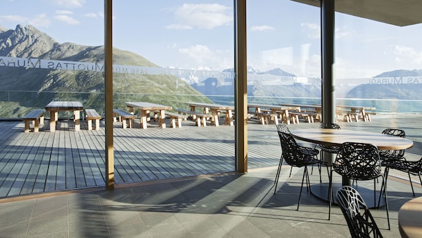 A terrace with wooden tables and chairs, overlooking a mountainous landscape.