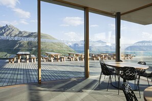 Una terraza con mesas y sillas de madera, con vistas a un paisaje montañoso.