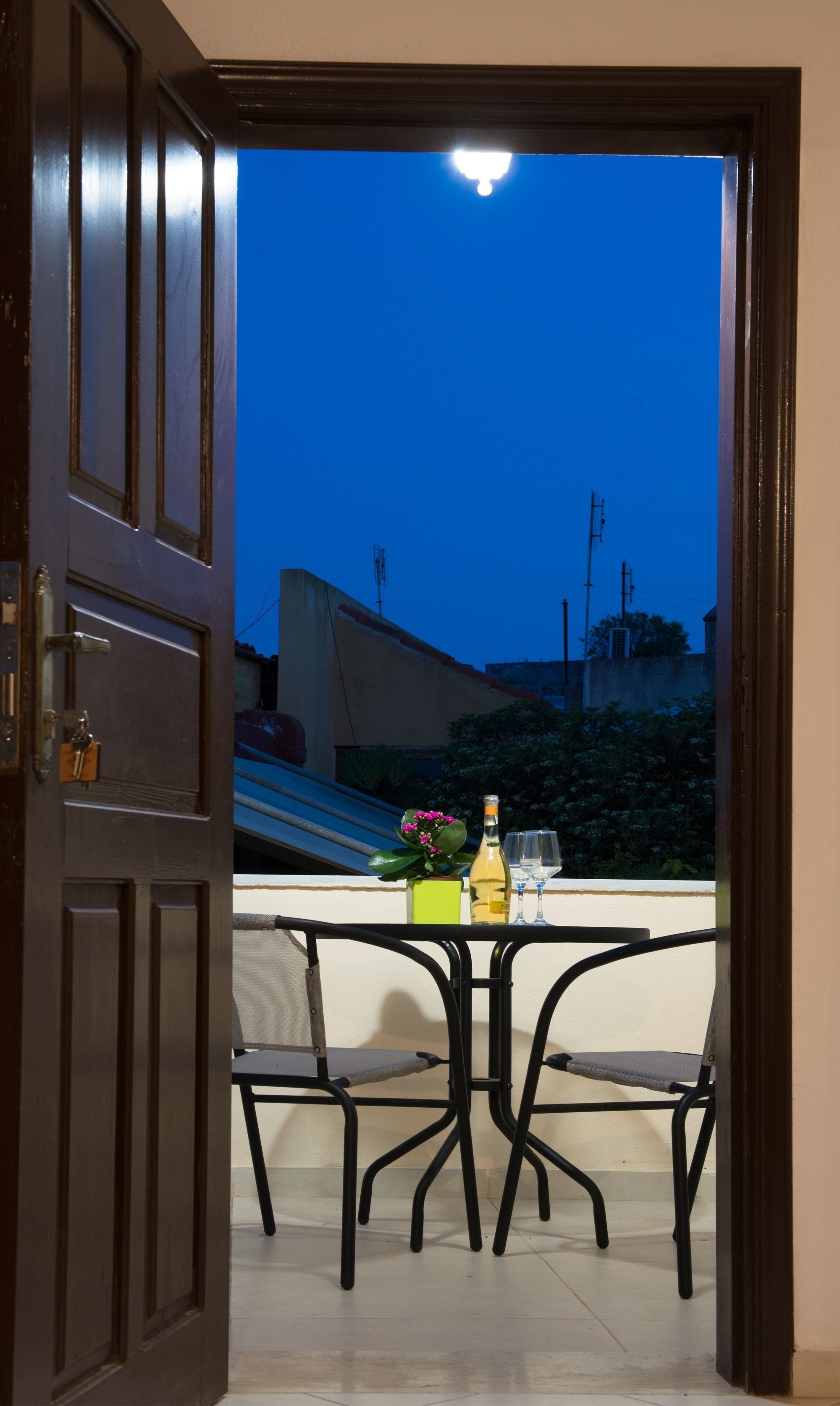 An open door leading to a balcony with a table, chairs, and a bottle of wine.