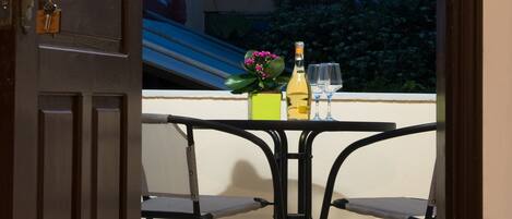 An open door leading to a balcony with a table, chairs, and a bottle of wine.