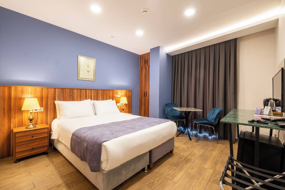 A hotel room with a bed, bedside tables, a desk, a chair, and a television.